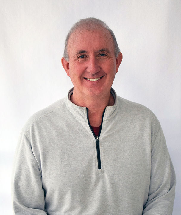 Man with gray hair smiling in gray pullover.