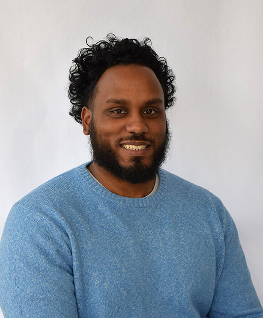 Man smiling in blue sweater against white background.