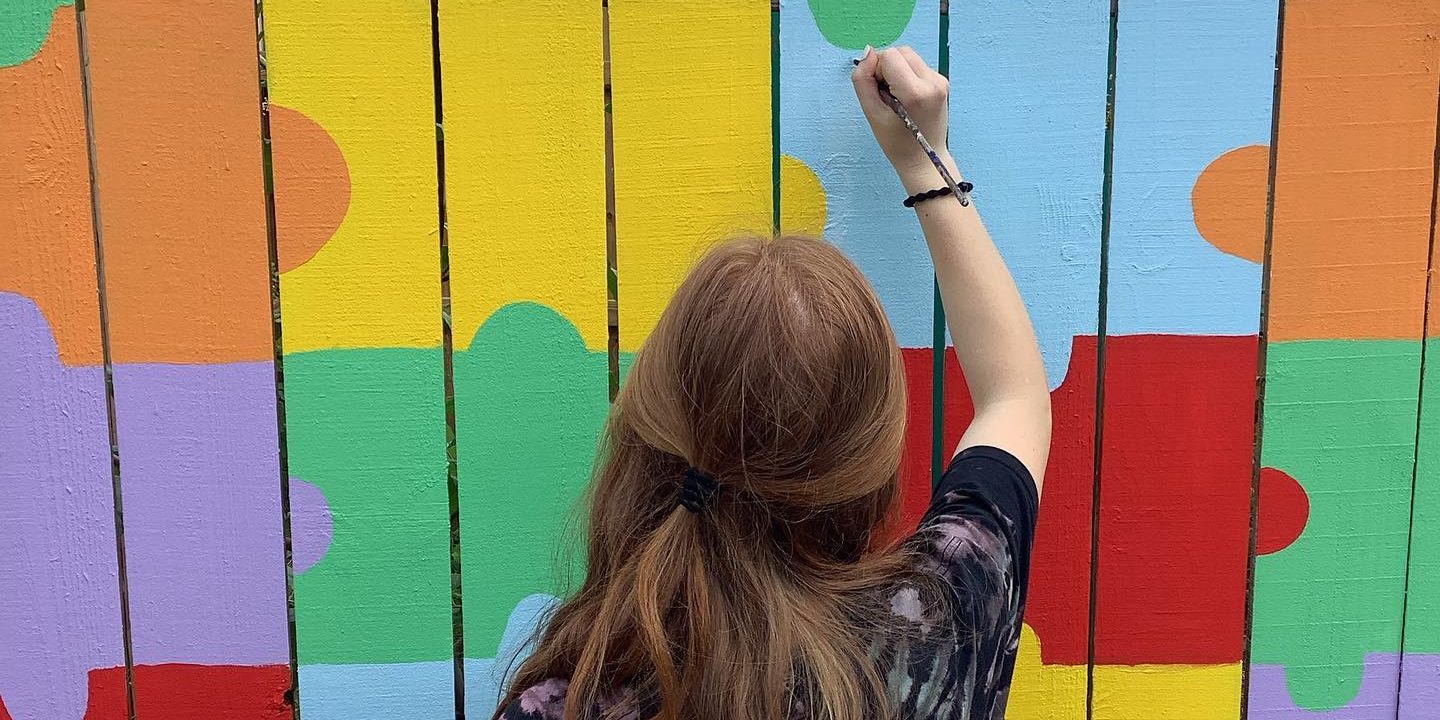 Woman painting a colorful puzzle-piece fence.
