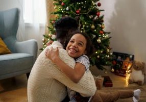 A smiling girl hugs a man by a Christmas tree