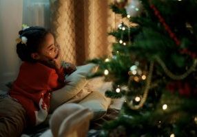 Girl in red sweater with butterfly clips by Christmas tree.