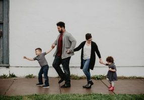 A happy family of four walking on a sidewalk, holding hands
