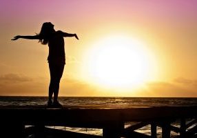 Silhouette of woman with arms outstretched at sunset on beach.