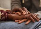 Hands of two people resting on top of the lap of a person in jeans